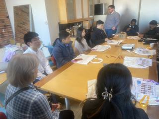 A speaker in conversation with participants around a table.